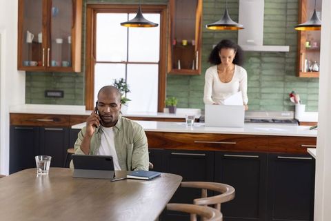 Diverse couple working from home in modern kitchen man using tablet and phone