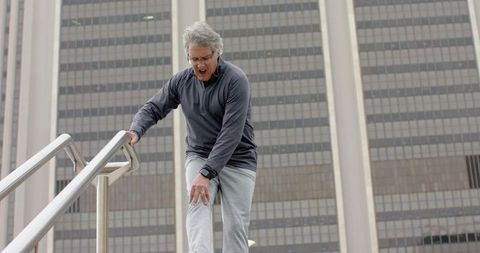 Older man clutching knee on urban stairs during outdoor workout