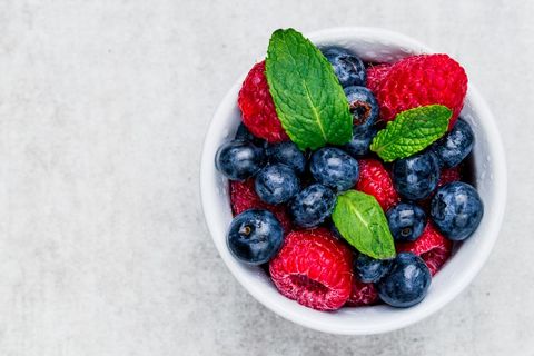 Serving fresh raspberries and blueberries with mint in white bowl top view