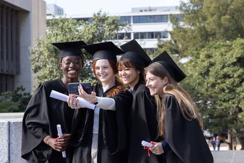Celebrating graduates taking selfie on campus while holding diplomas