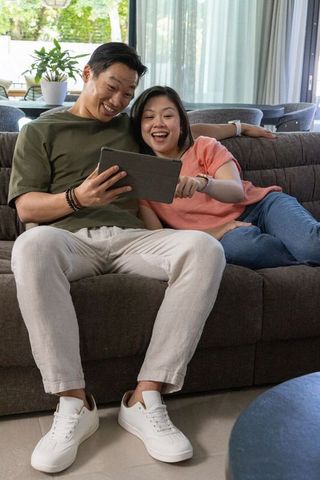 Happy couple relaxing and sharing tablet on gray sofa in bright modern living room