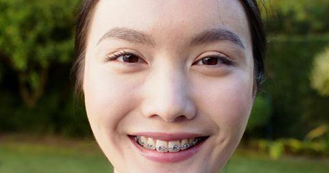 Woman Smiling with Braces in Sunlit Garden Setting