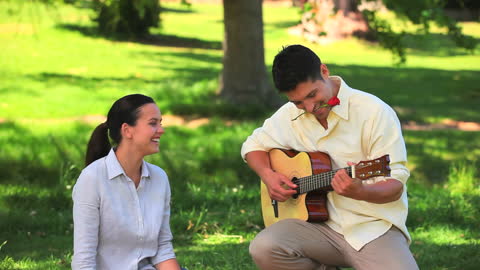 Man Serenading Wife in Park with Guitar on a Sunny Day