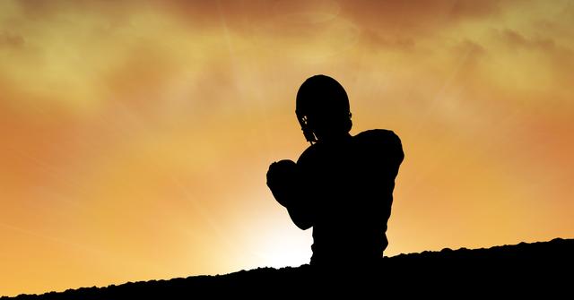 Silhouette of an American football player with a helmet against a vibrant orange sunset sky. This photo captures the essence of dedication, strength, and athleticism in the sport. Ideal for use in sports magazines, athletic brand advertising, motivational posters, or team events.