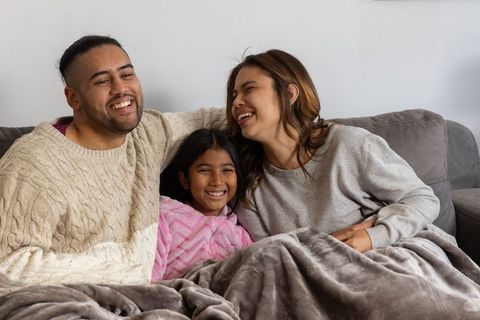 Cozy family cuddling on couch under plush blanket laughing and smiling together at home