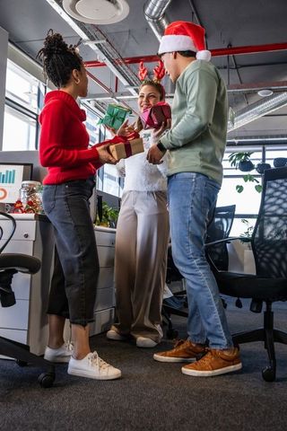Diverse coworkers exchanging holiday gifts and celebrating in modern open-plan office