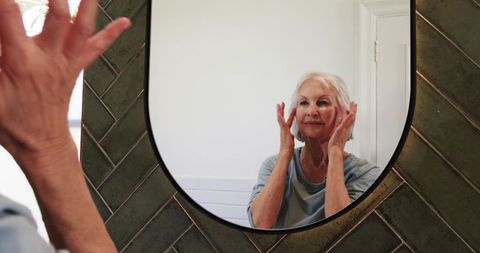 Senior woman applying facial cream through bathroom mirror reflection