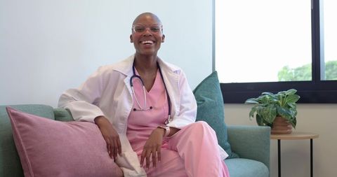 Smiling african american female clinician relaxing on sofa in clinic wearing pink scrubs