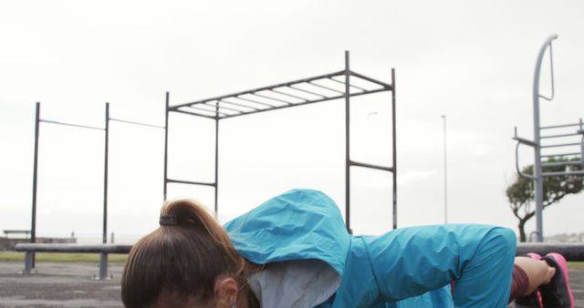 Woman performing workout routine in urban fitness park. Woman is engaged in an outdoor fitness activity focusing on muscle strengthening. Fitness park provides a public space for physical exercise. Useful for promoting outdoor fitness, healthy lifestyles, urban fitness programs, and public recreational spaces.