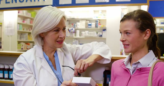A pharmacist with grey hair assisting a young woman at the counter, holding a prescription box. Shelves full of medications are visible in the background. This can be used in promotional materials for pharmacies, healthcare advertisements, or educational content about obtaining prescriptions.
