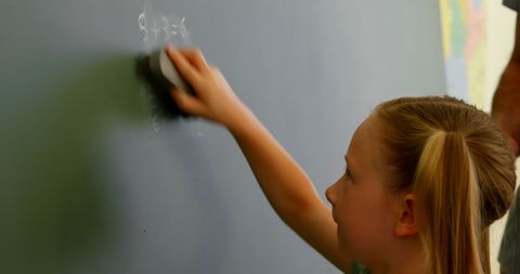 Young schoolgirl erasing math equations from blackboard