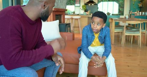 African american father talking with son on sofa in open-plan home