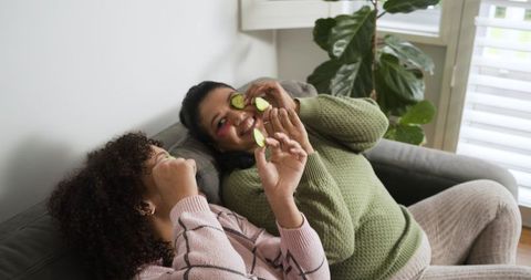 African american women relaxing on couch with cucumber slices over eyes enjoying self care