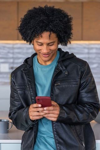 African american man smiling while texting on red smartphone in modern cafe interior