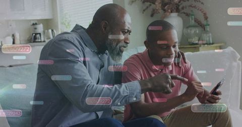 Father guiding teenage son using smartphone on cozy living room couch for tech learning