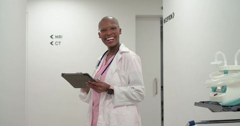 Smiling african american woman doctor holding tablet in hospital imaging corridor