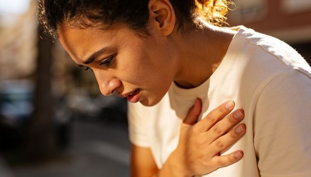 Young woman clutching chest leaning on sunlit city sidewalk during golden hour