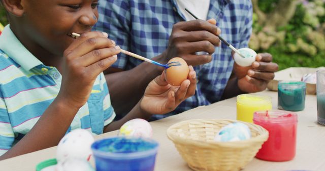 Father and son enjoying time together, painting Easter eggs with various colorful paints. Suitable for family, holiday, Easter traditions, parenting blogs, and creative activity promotions.