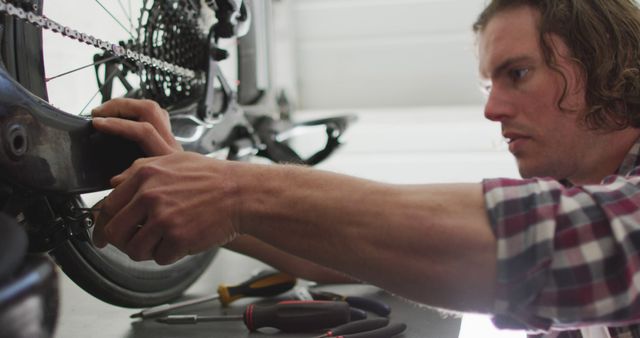 A professional mechanic is focused on repairing a bicycle in a workshop. Various hand tools are visible on the table, indicating a detailed maintenance process. This image is ideal for use in articles or advertisements related to bicycle repair services, professional workshops, or maintenance guides.