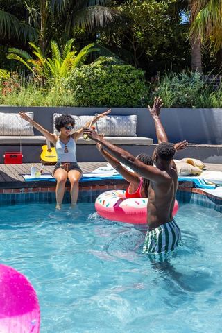 African american friends laughing and splashing in sunny backyard pool with donut float