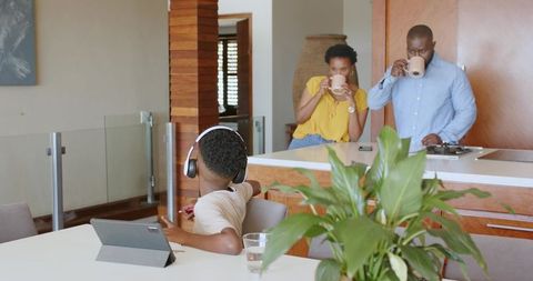 African American family enjoying morning coffee in modern kitchen while child using tablet