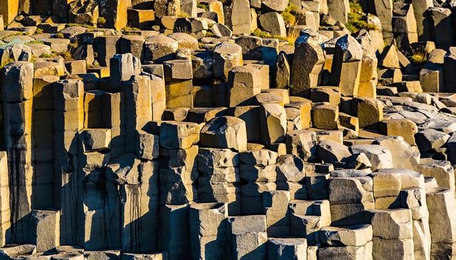 Sunlit columnar basalt hexagonal pillars on coastal cliff, geological rock formation