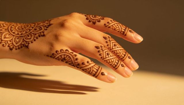 Hand wearing intricate henna mandala on dorsal fingers with warm light and shadow