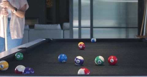 Modern game room with black pool table and scattered billiard balls, player holding cue