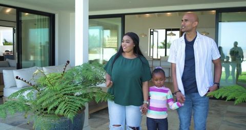 African american family walking hand in hand on modern home patio with lush potted fern