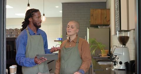 Baristas collaborating behind counter using tablet in modern industrial coffeehouse