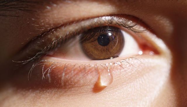 Glistening teardrop on brown eye closeup conveying emotion and delicate skin texture