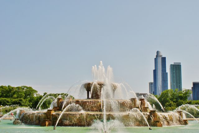 Image depicts a stunning fountain with flowing water jets set against a backdrop of tall skyscrapers, embodying a beautiful blend of nature and urban development. Suitable for use in projects related to urban parks, architectural beauty, travel destinations, and city planning aesthetics.