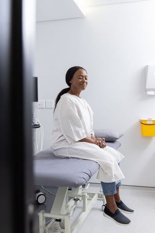 Patient sitting on exam table wearing clinic gown, waiting calmly in bright medical room