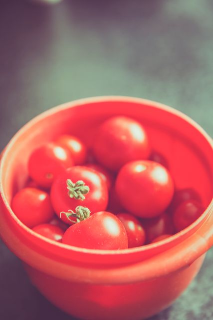 Fresh cherry tomatoes in red bowl, perfect for illustrating healthy eating, gardening blogs, summer recipes, and cookbooks. Soft focus adds an artistic touch, suitable for food blogs and decor articles.