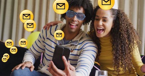 Couple laughing while checking incoming messages on smartphone during home party
