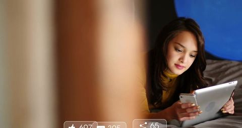 Reclining Woman Navigating Digital Devices in Cozy Bedroom