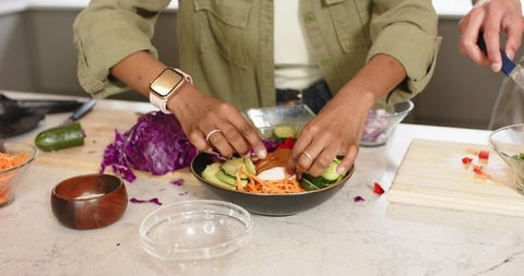 Couple preparing vibrant salad bowl with avocado, shredded cabbage and cucumber