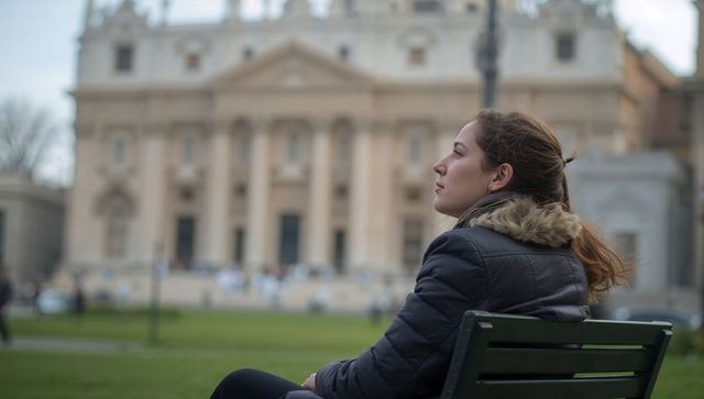 Young woman sitting on bench gazing at historic cathedral facade in city park plaza