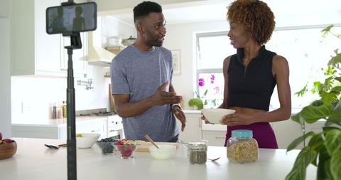 African American couple filming healthy smoothie bowl recipe in bright modern kitchen