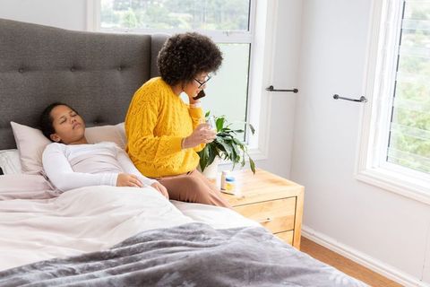 African american caregiver giving medicine to sleeping child on bed while calling on phone