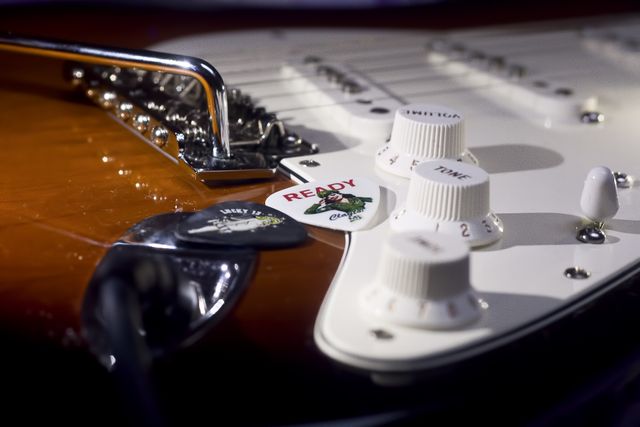 This image captures a detailed close-up of an electric guitar's knobs, strings, bridge, and picks, including one labeled 'READY.' Useful for music-related content, promotions for musical gear, rock band posters, and learning resources for guitar enthusiasts.