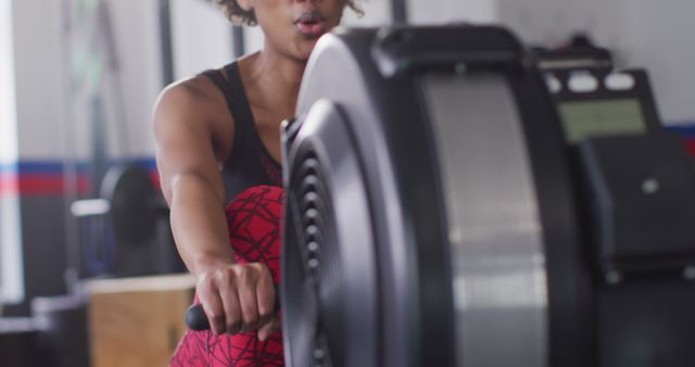 Image of determined african american woman using rowing machine working out at gym. Exercise, fitness and healthy lifestyle.