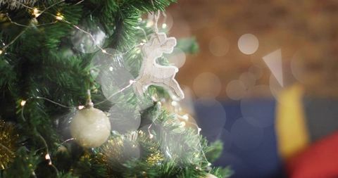 Hanging wooden reindeer ornament on christmas tree with warm bokeh lights and tinsel