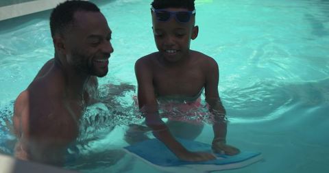 African american father teaching son with kickboard in backyard pool, summer family bonding