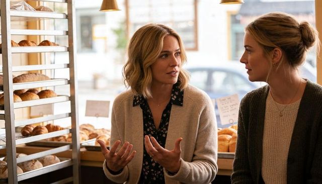 Women chatting at cozy bakery counter wearing cardigans, fresh croissants, warm daylight