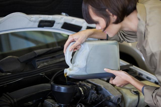 Female mechanic pouring oil lubricant into car engine at garage. Ideal for content related to automotive maintenance, car repair services, professional mechanics, and DIY car care tutorials.