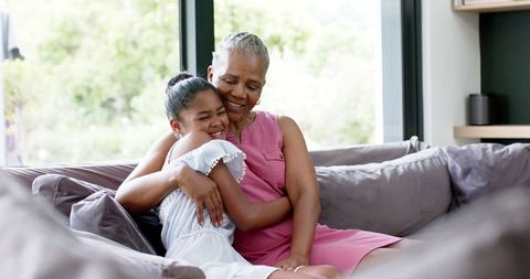 Grandmother and Granddaughter Embracing on Comfortable Sofa