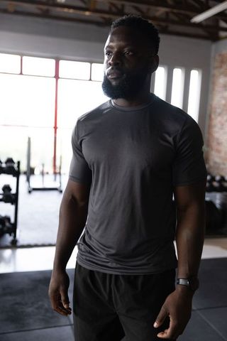 African american athlete training in industrial gym with red windows and dumbbell rack