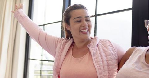African american woman laughing and leaning toward friend in pink vest bright living room
