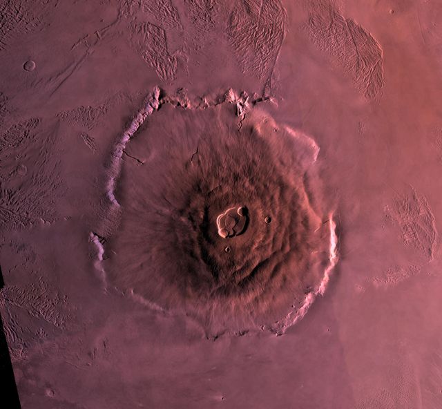 Image shows Olympus Mons on Mars, the largest known volcano in the Solar System, towering 27 kilometers high with a base over 600 kilometers wide. The caldera, almost 3 kilometers deep and 25 kilometers across, dominates the summit. The surrounding lava flows and the ridged and grooved 'aureole' surrounding the plains offer a striking view. This image can be used in educational materials about planetary geology, space exploration, and comparisons of planetary landscapes in the Solar System.